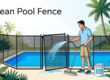 A mesh pool fence is rinsed beside a blue pool with a hose, brush, and soap bucket.
