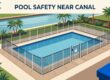 A fenced backyard pool sits beside a landscaped canal with palm trees.